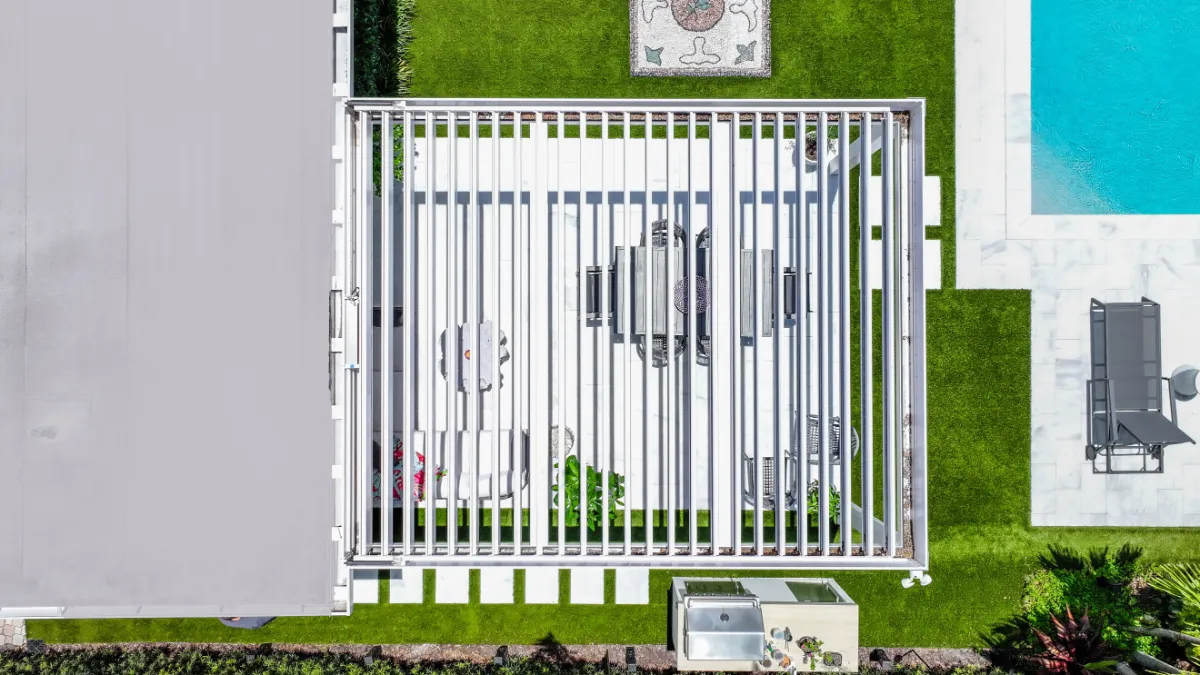 Aerial view of a smart louvered pergola with open louvers revealing a furnished patio beside a pool and outdoor kitchen