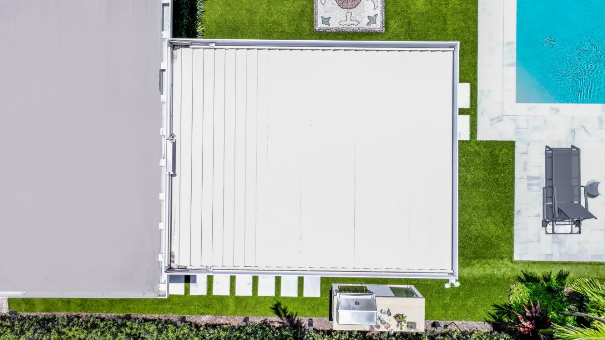 Aerial view of an automated pergola with closed louvers beside a modern pool and outdoor kitchen