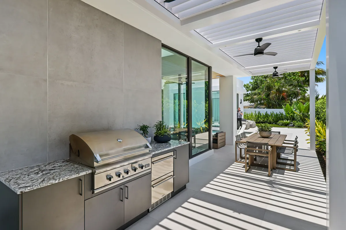 Contemporary outdoor kitchen and dining area shaded by a modern pergola with a motorized louvered roof.