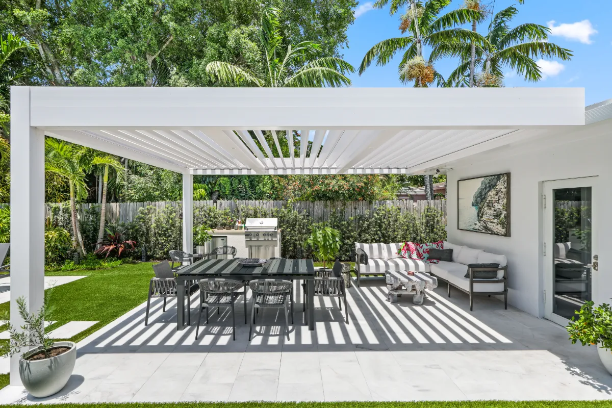 Smart pergola with partially open louvers shading a modern patio featuring dining and lounge areas in a lush backyard.