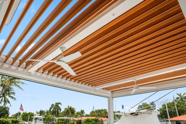 Close-up view of R-Blade pergola wood slat ceiling with integrated ceiling fans, showing craftsmanship and architectural details against blue sky