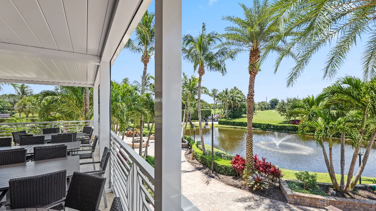 View from Jonathan’s Landing’s pergola-covered dining area overlooking palm trees, a pond, and the golf course beyond.