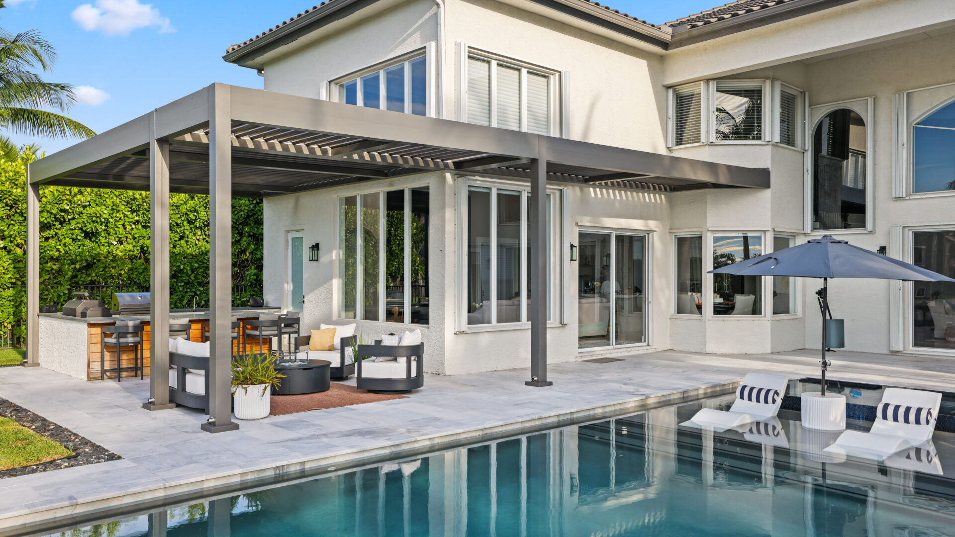 L-shaped pergola with motorized louvers covering outdoor kitchen and lounge beside modern poolside patio.