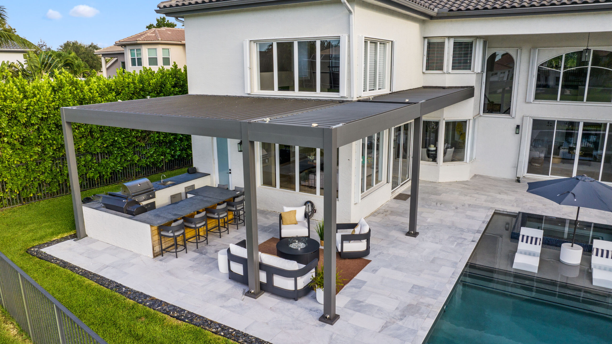 Luxury backyard with louvered pergola, outdoor kitchen, seating area, and pool in Florida.