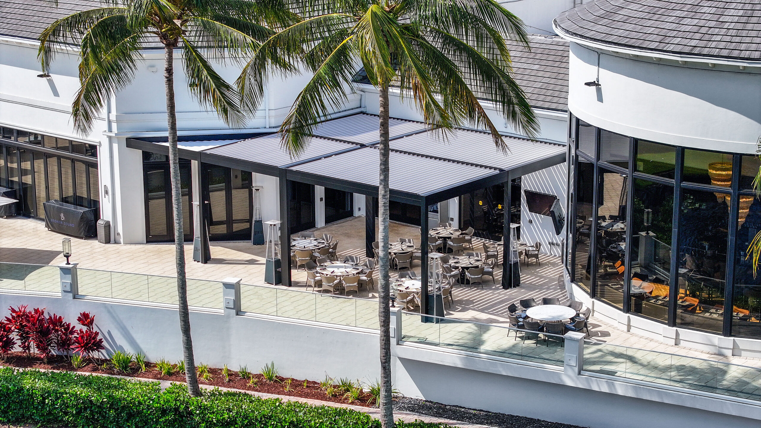 Covered outdoor dining area with aluminum pergola at luxury clubhouse in South Florida, featuring motorized louvers.