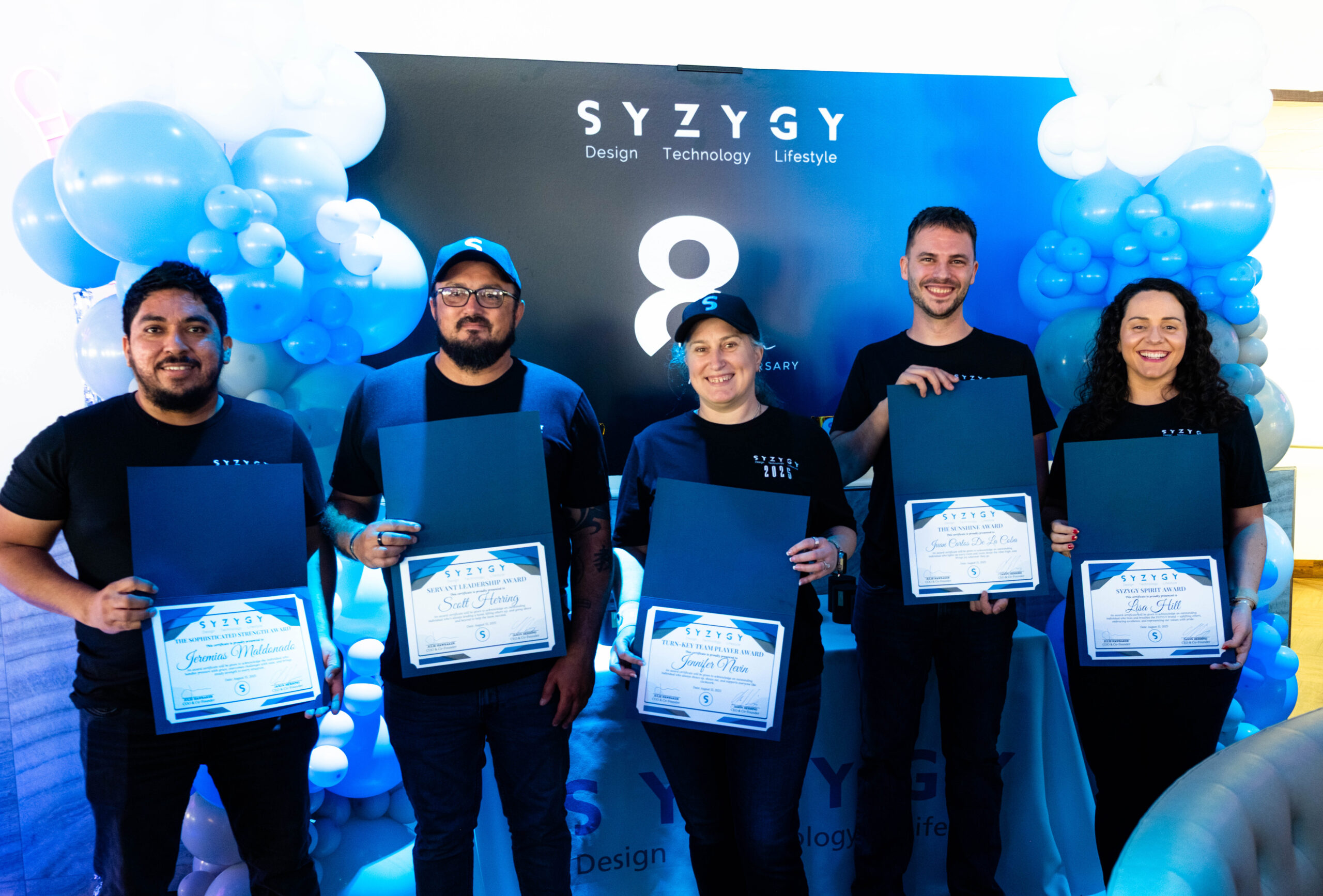 SYZYGY Global team members holding anniversary award certificates during the 8th anniversary celebration.