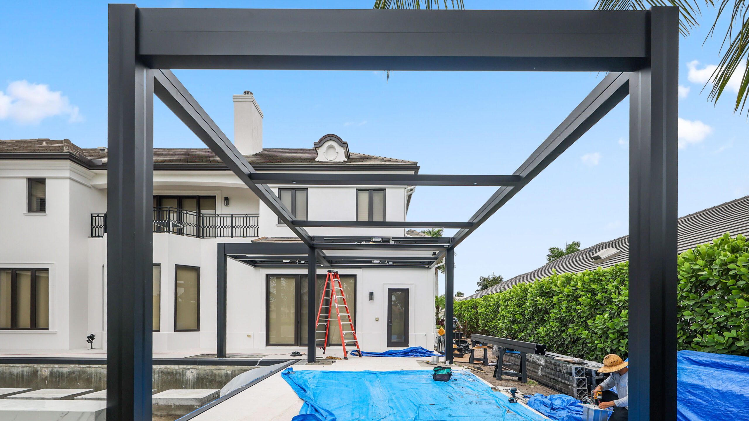 Construction of a modern L-shaped pergola with an aluminum frame beside a luxury home and pool.