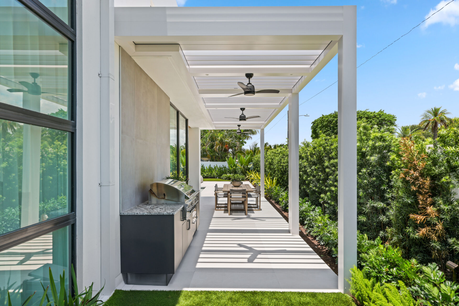 White louvered pergola shades an outdoor kitchen and dining area, showcasing modern design and durable construction.