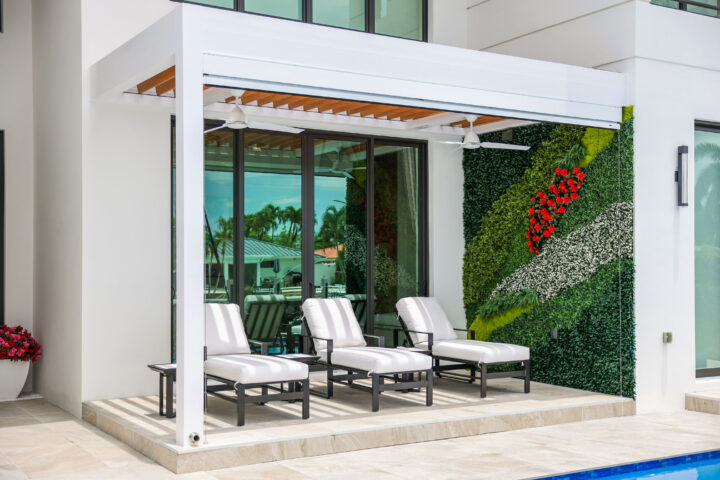 Modern pergola with white louvers shades a patio with lounge chairs beside a pool and living green wall.
