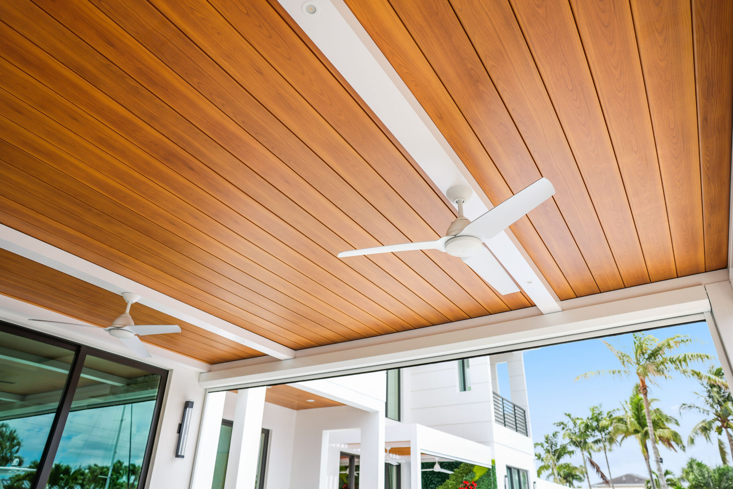 Close-up of a wood-grain aluminum patio ceiling with modern white ceiling fans and clean architectural lines.