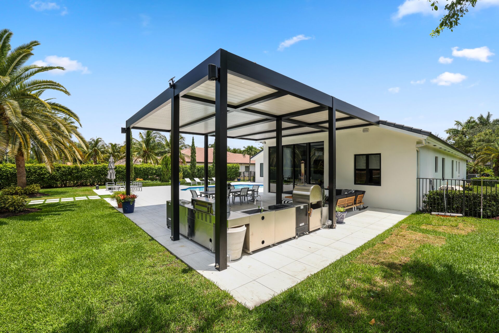 Black aluminum pergola with white louvers shades an outdoor kitchen and patio area, blending style with durability.
