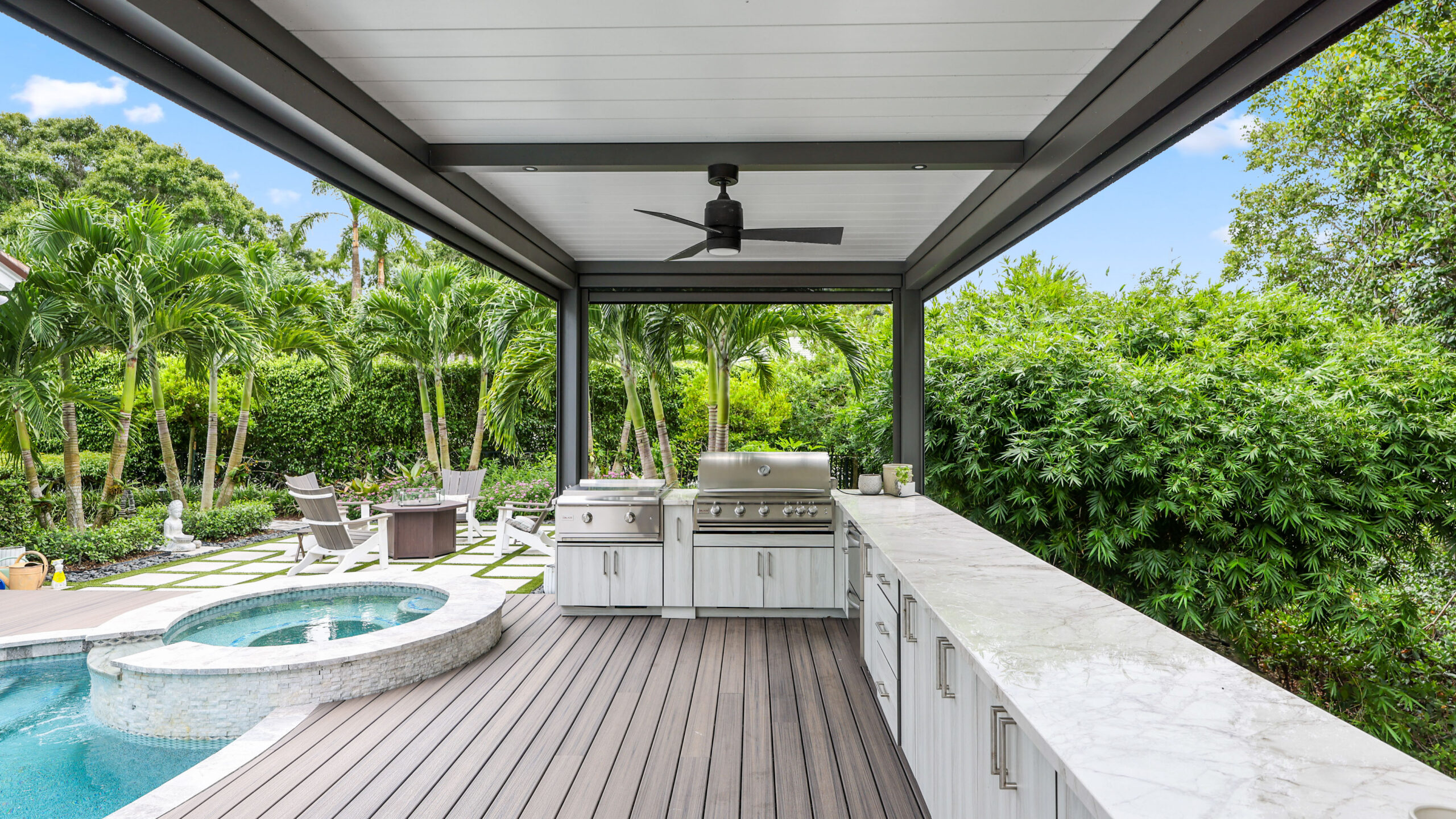 L-shaped pergola with insulated roof shading luxury outdoor kitchen and grill area beside pool and spa.