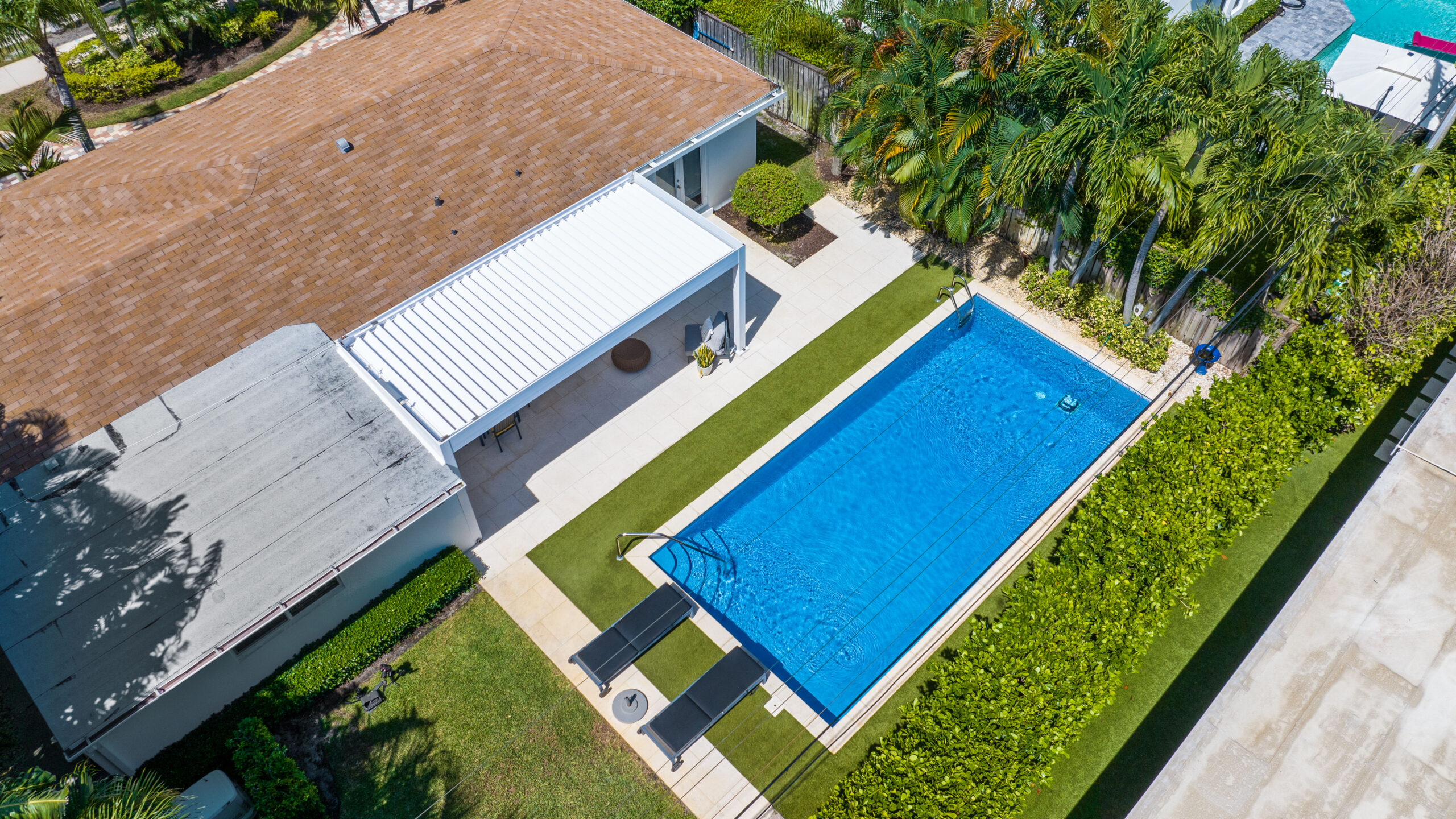 Aerial view of white lean-to pergola covering a poolside patio at a South Florida home.