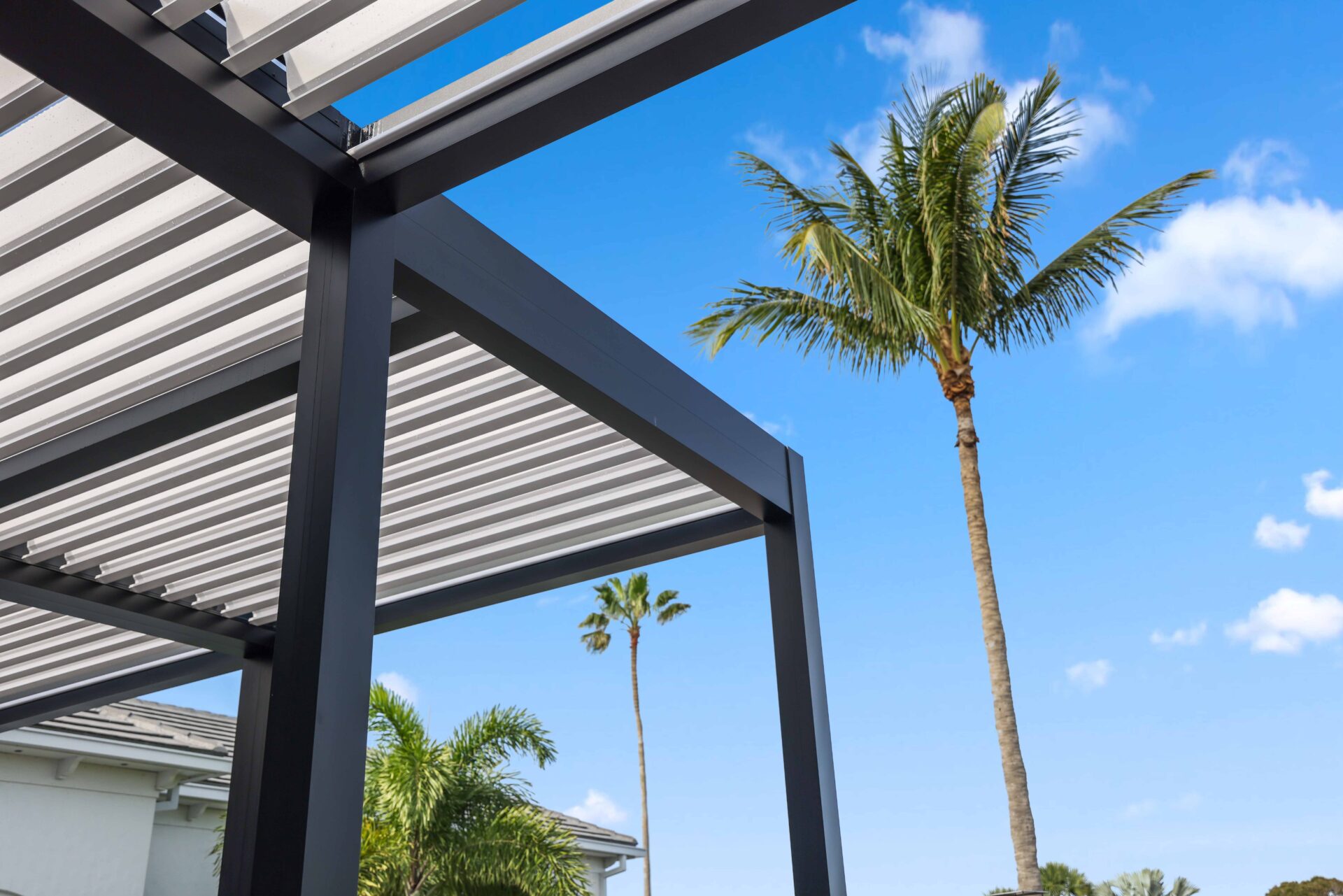 Detail view of R-Blade pergola frame and louvers at Broken Sound Club with palm trees and blue sky in the background.