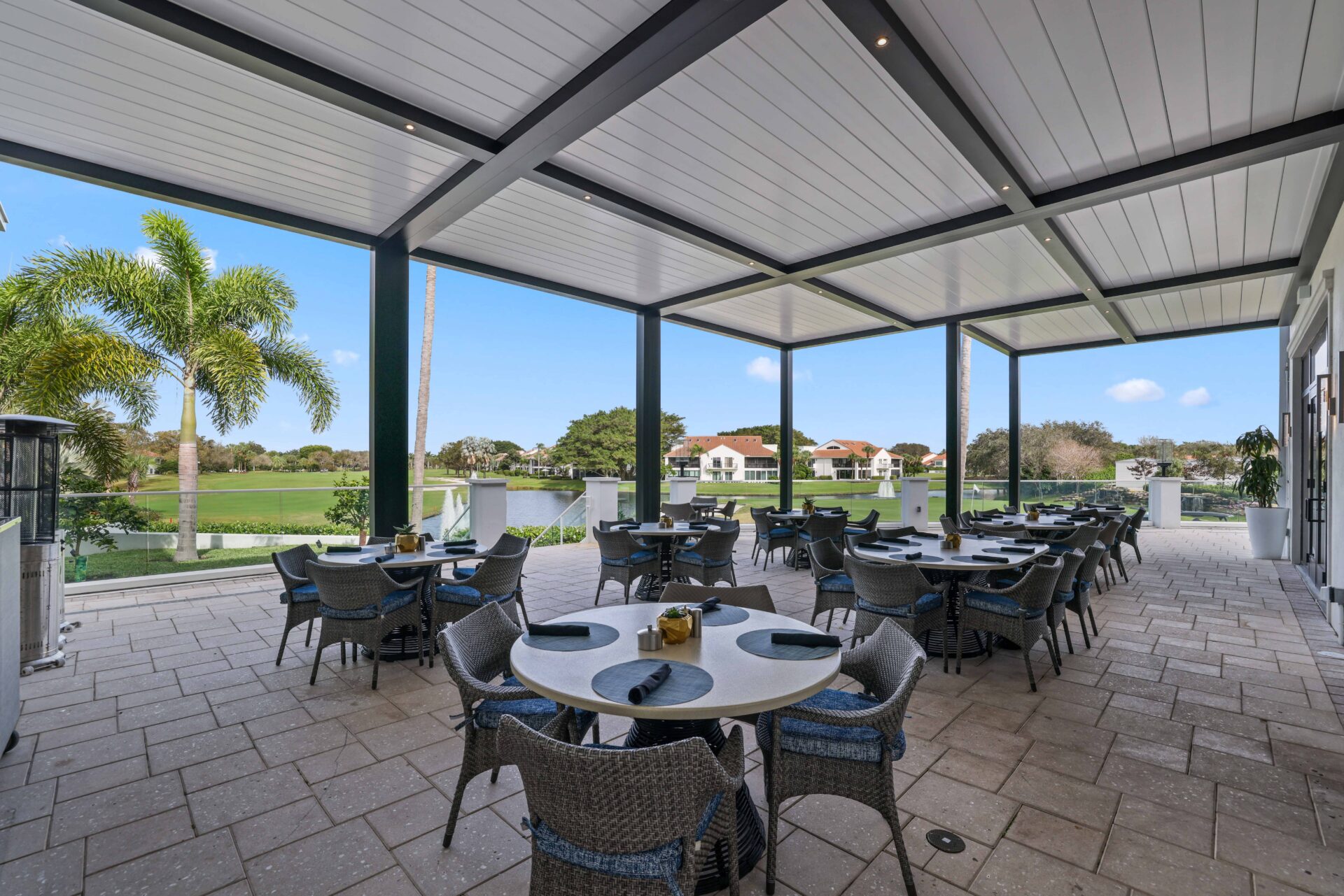 Shaded dining area under R-Blade pergolas at Broken Sound Club, overlooking golf course and water views.