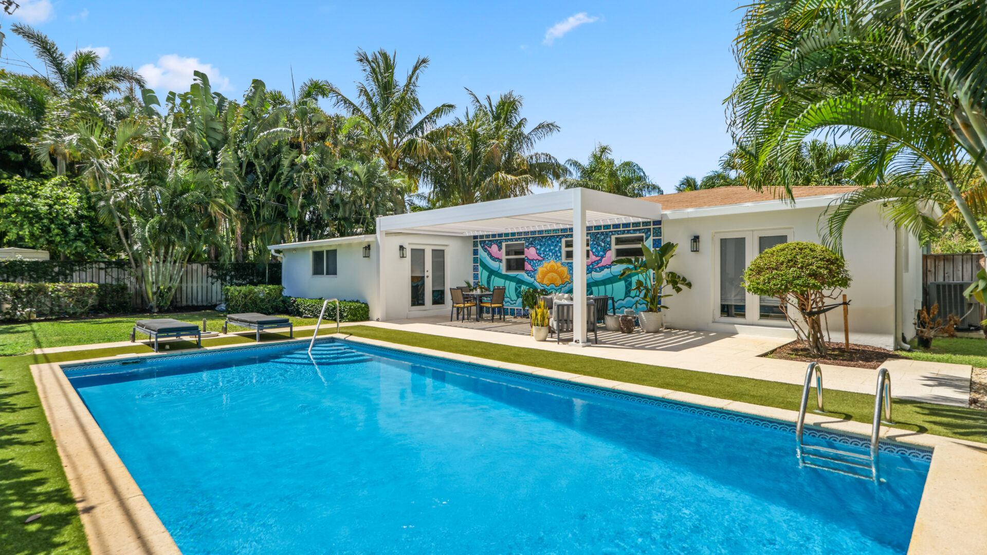 White lean-to pergola providing poolside shade for a colorful backyard patio in South Florida.