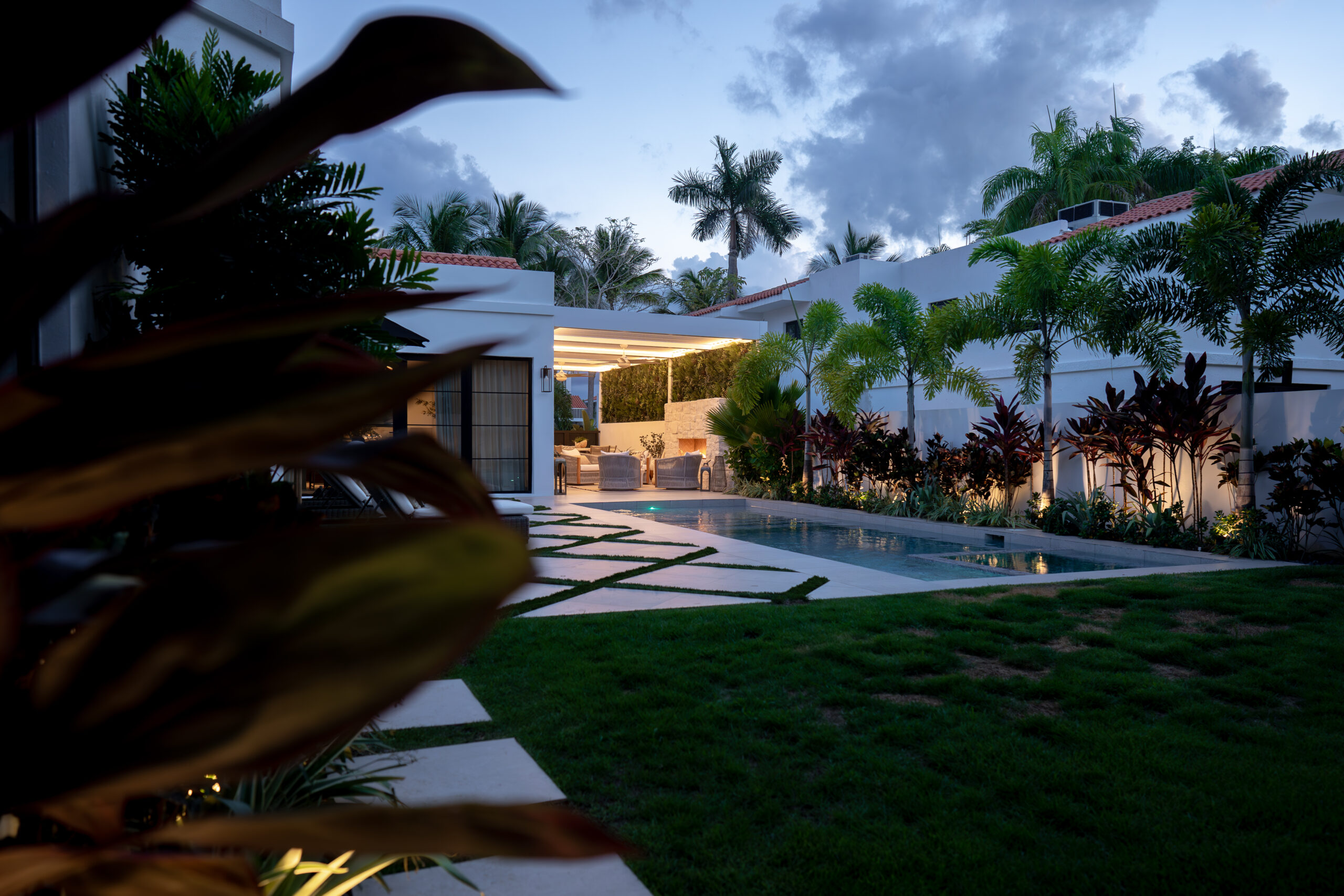 Luxury backyard with a R-BLADE pergola featuring integrated LED lighting, clean lines, and a seamless poolside design surrounded by tropical landscaping.