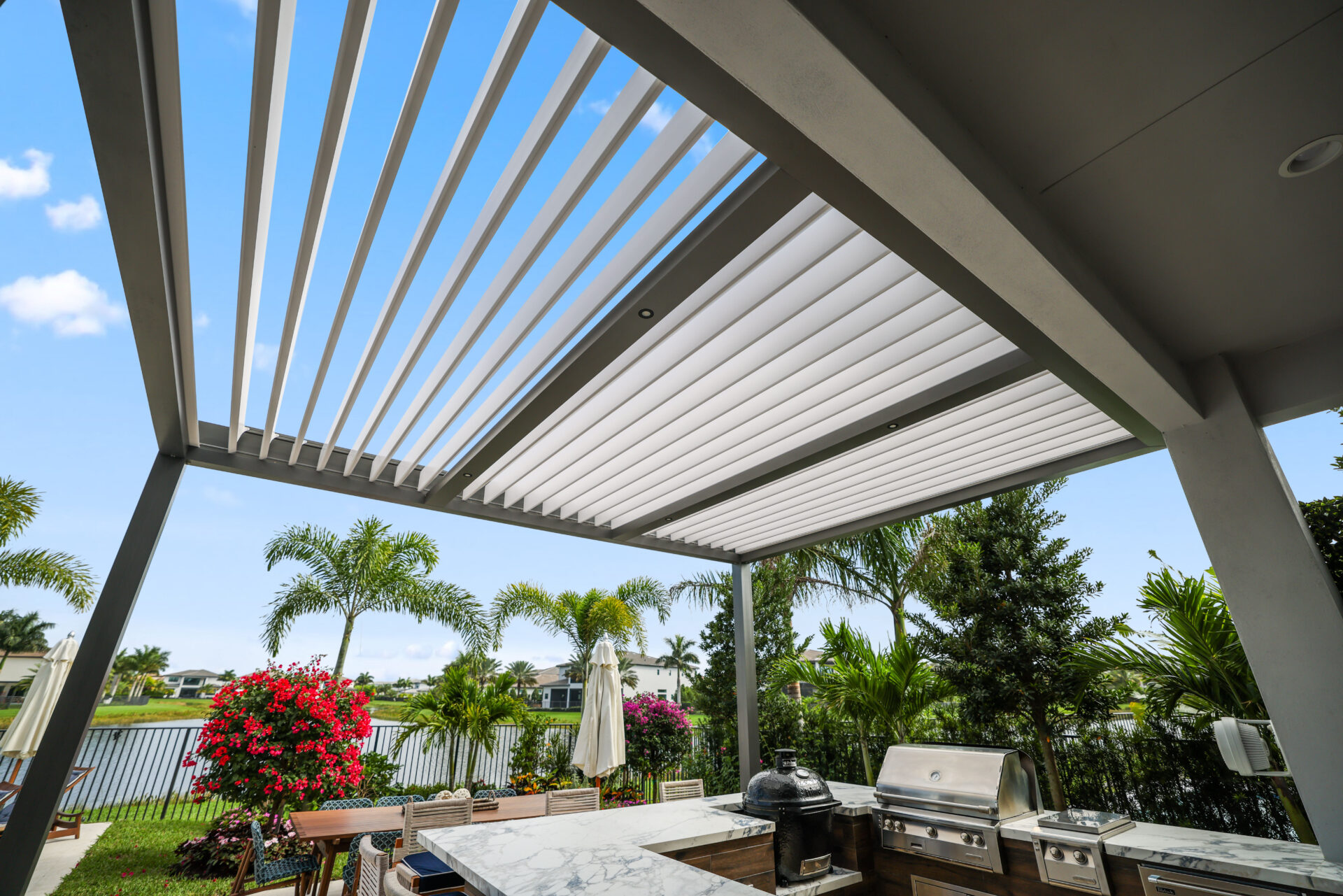 Close-up of R-Blade pergola louvers above an outdoor kitchen with marble counters and stainless steel appliances.
