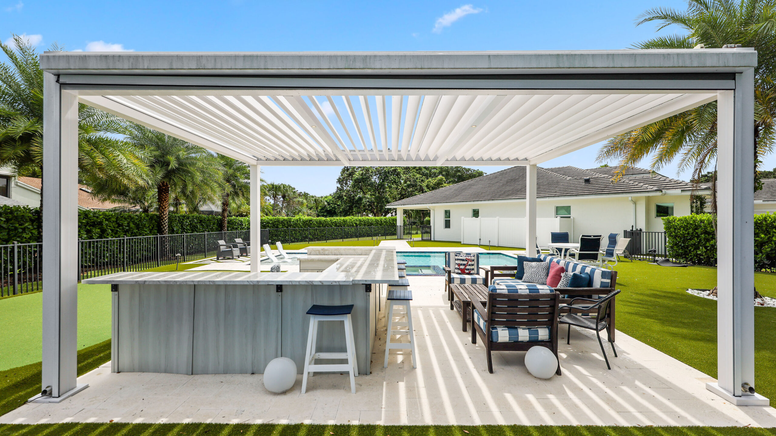 Modern poolside lounge with sloped pergola roof, outdoor kitchen, TV, and contemporary seating area.