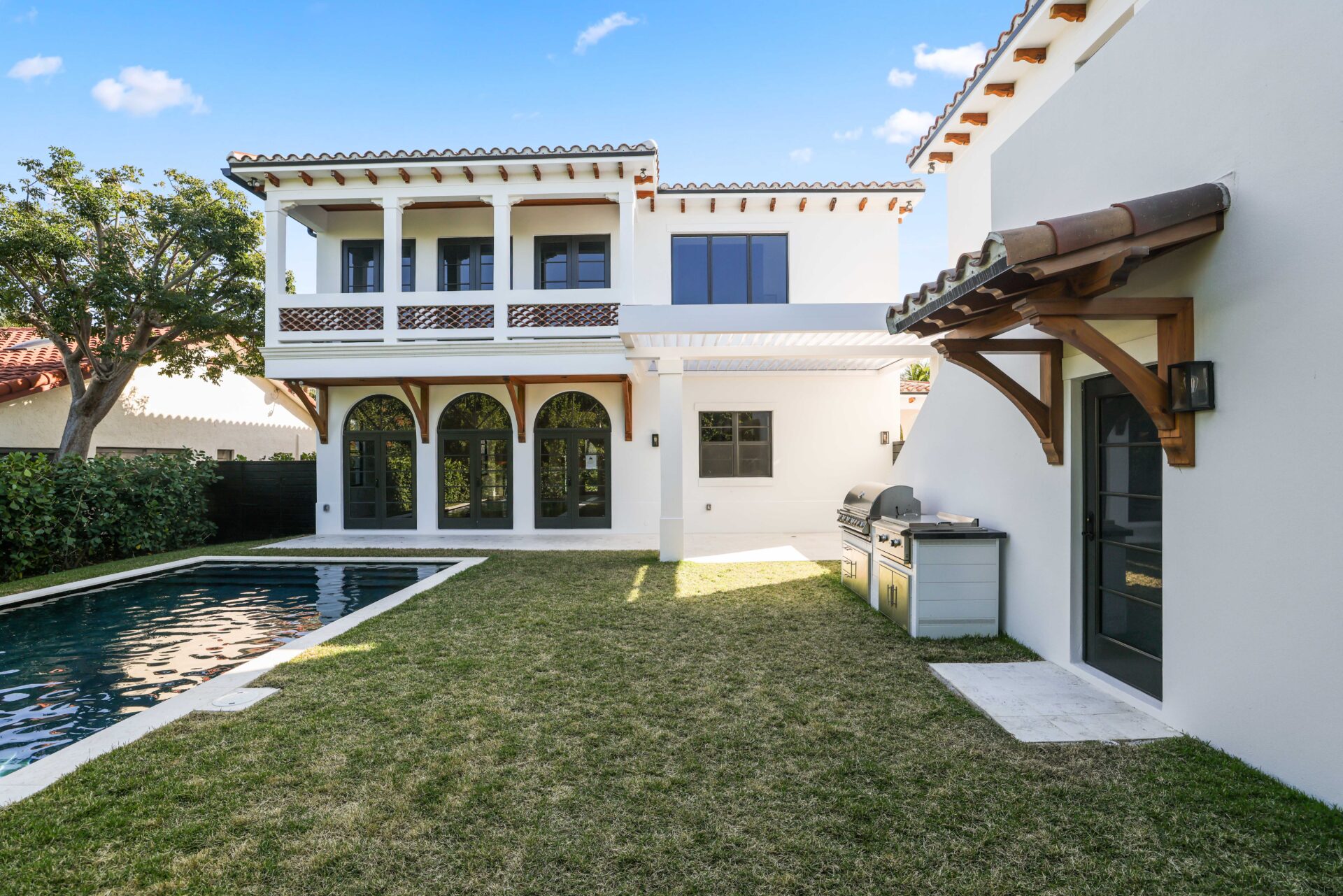 Mediterranean-style backyard with arched loggia, modern pergola, outdoor kitchen, and pool at a luxury Florida home.