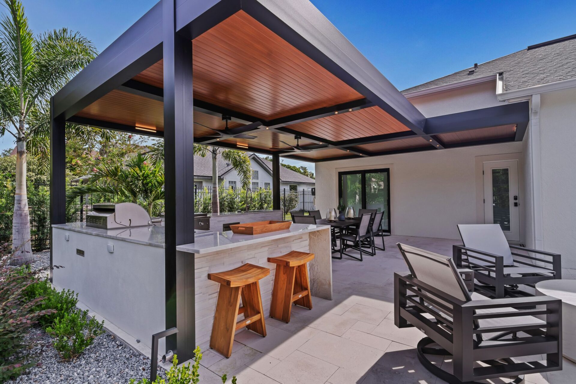 Modern insulated roof pergola with wood-look ceiling over outdoor kitchen and dining area.