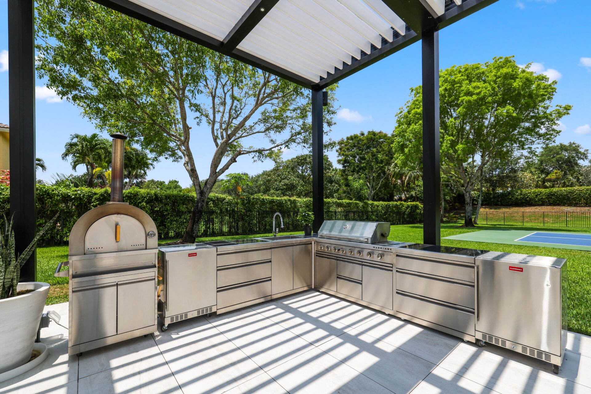 Outdoor kitchen with stainless appliances beneath black aluminum pergola.