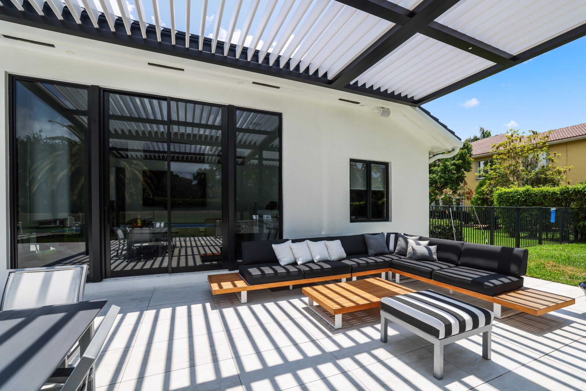 Black pergola with adjustable louvers shading modern patio seating and glass doors.