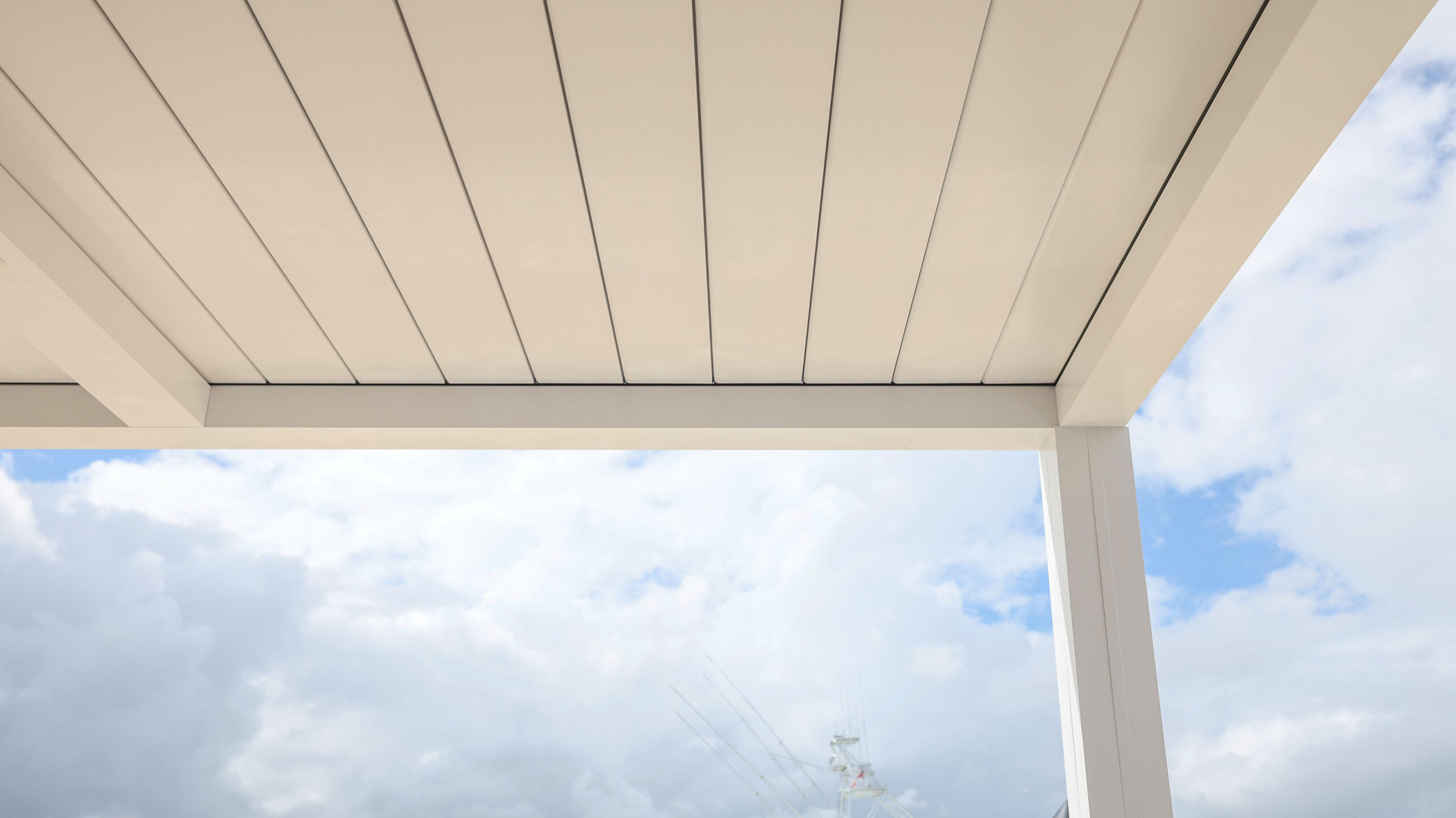 Close-up of white aluminum pergola roof panels with clean modern lines set against a bright cloudy sky.