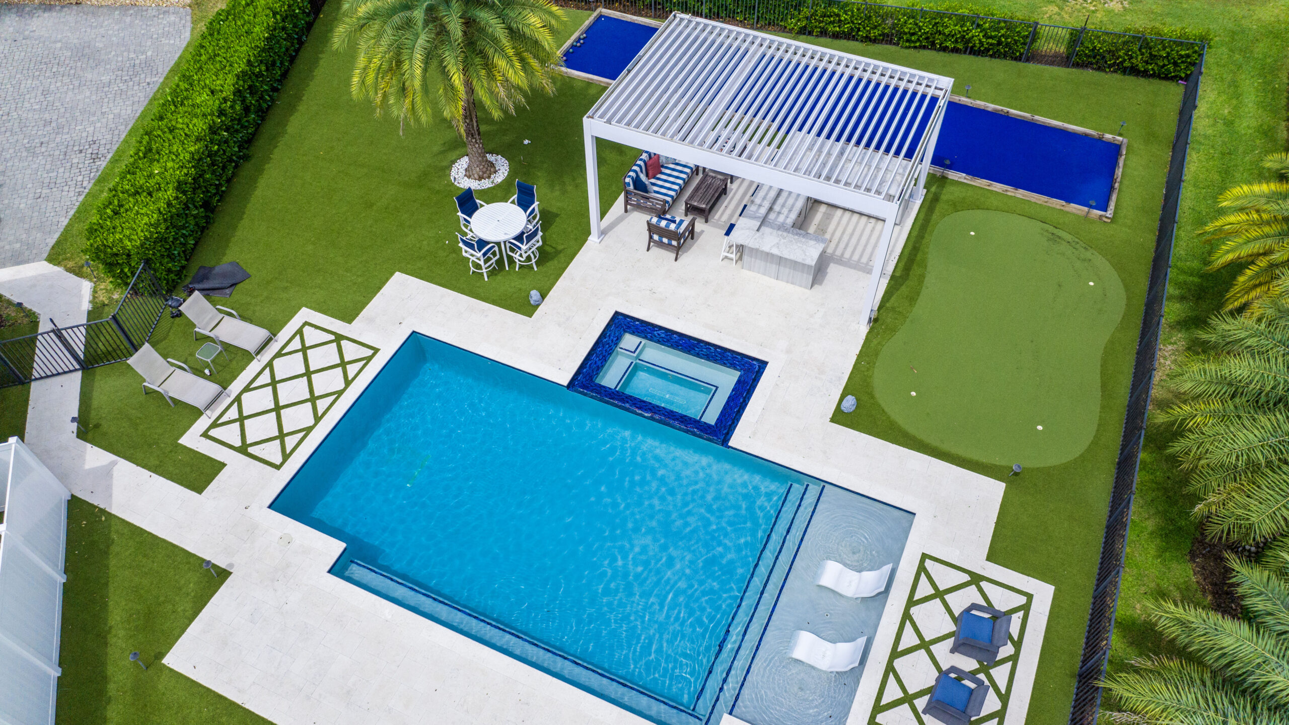 Aerial view of a large aluminum pergola beside a luxury pool and putting green in a modern Florida backyard.