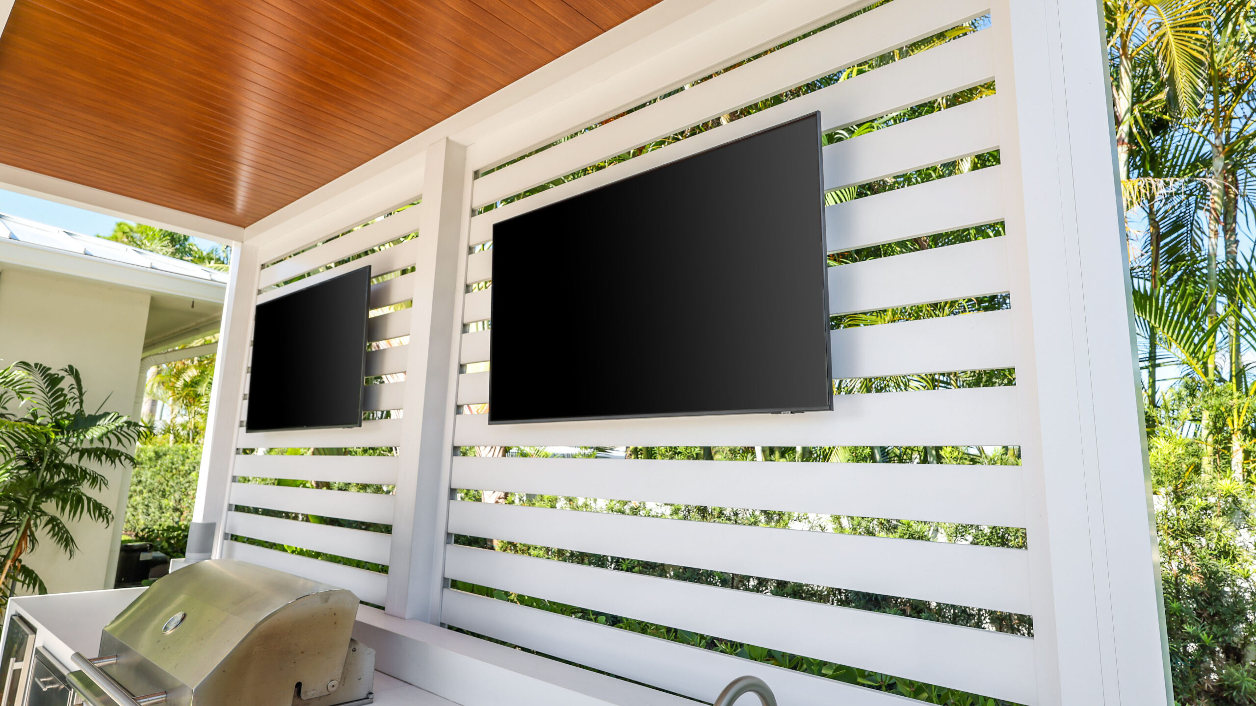 Close-up of a modern pergola privacy wall with mounted outdoor TVs above a built-in grill station.