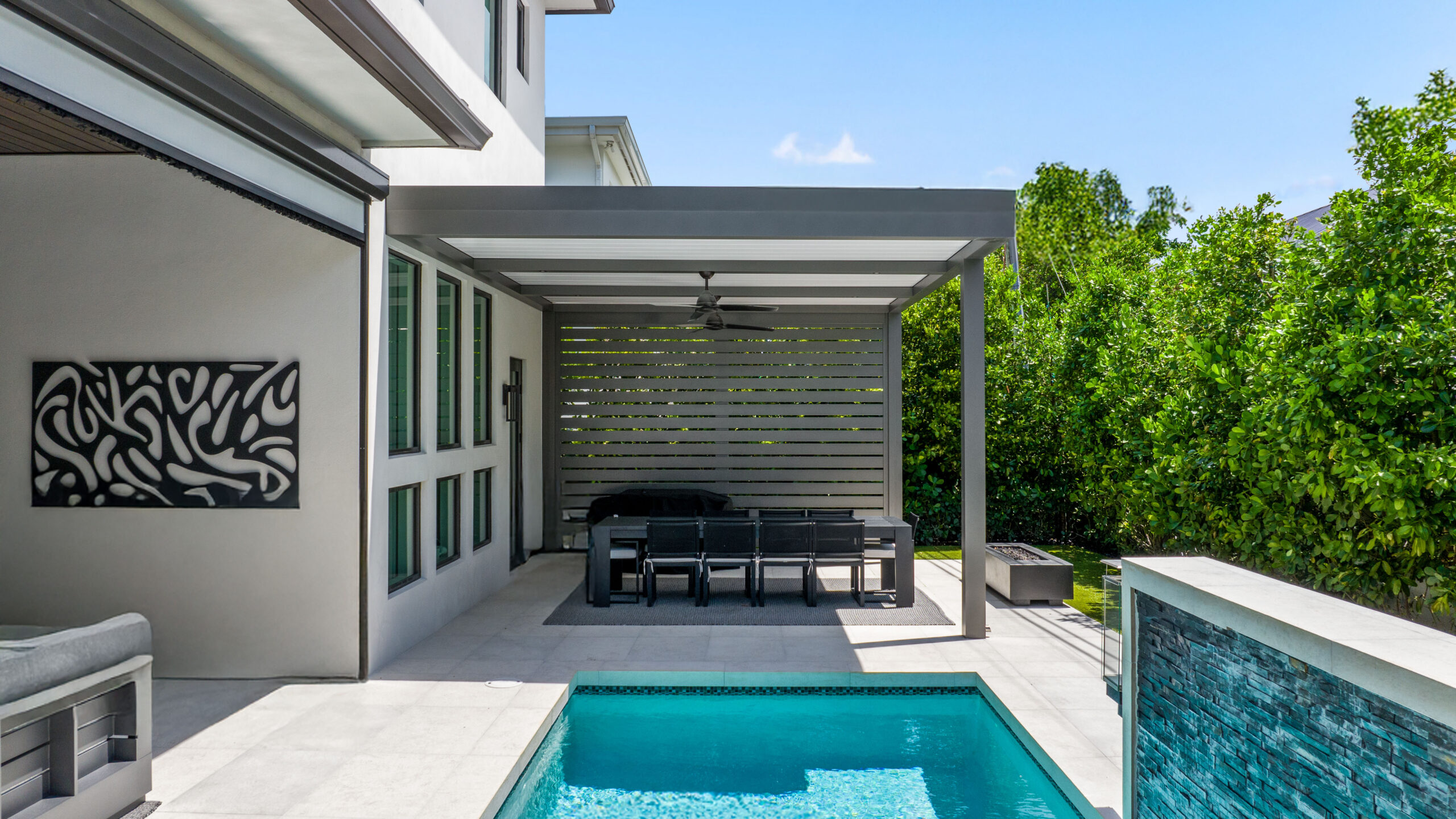Modern aluminum pergola with a privacy wall shading a poolside dining area in a South Florida backyard.