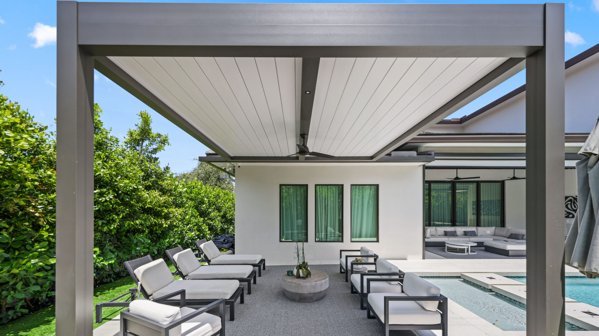 Modern aluminum pergola with a louvered roof shading a poolside lounge area in a South Florida backyard.