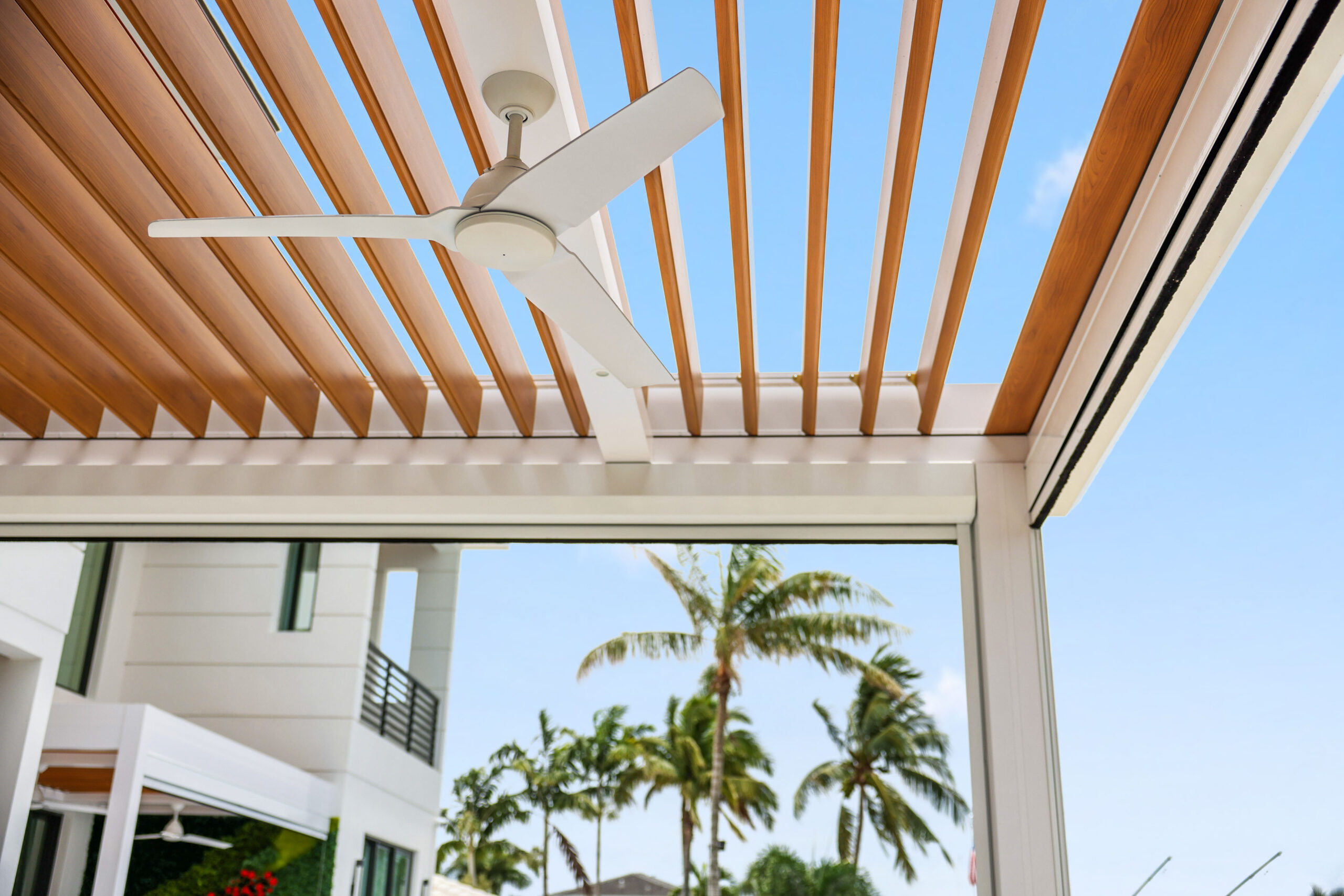 Close-up of woodgrain aluminum pergola louvers with integrated fan, designed for coastal outdoor living.