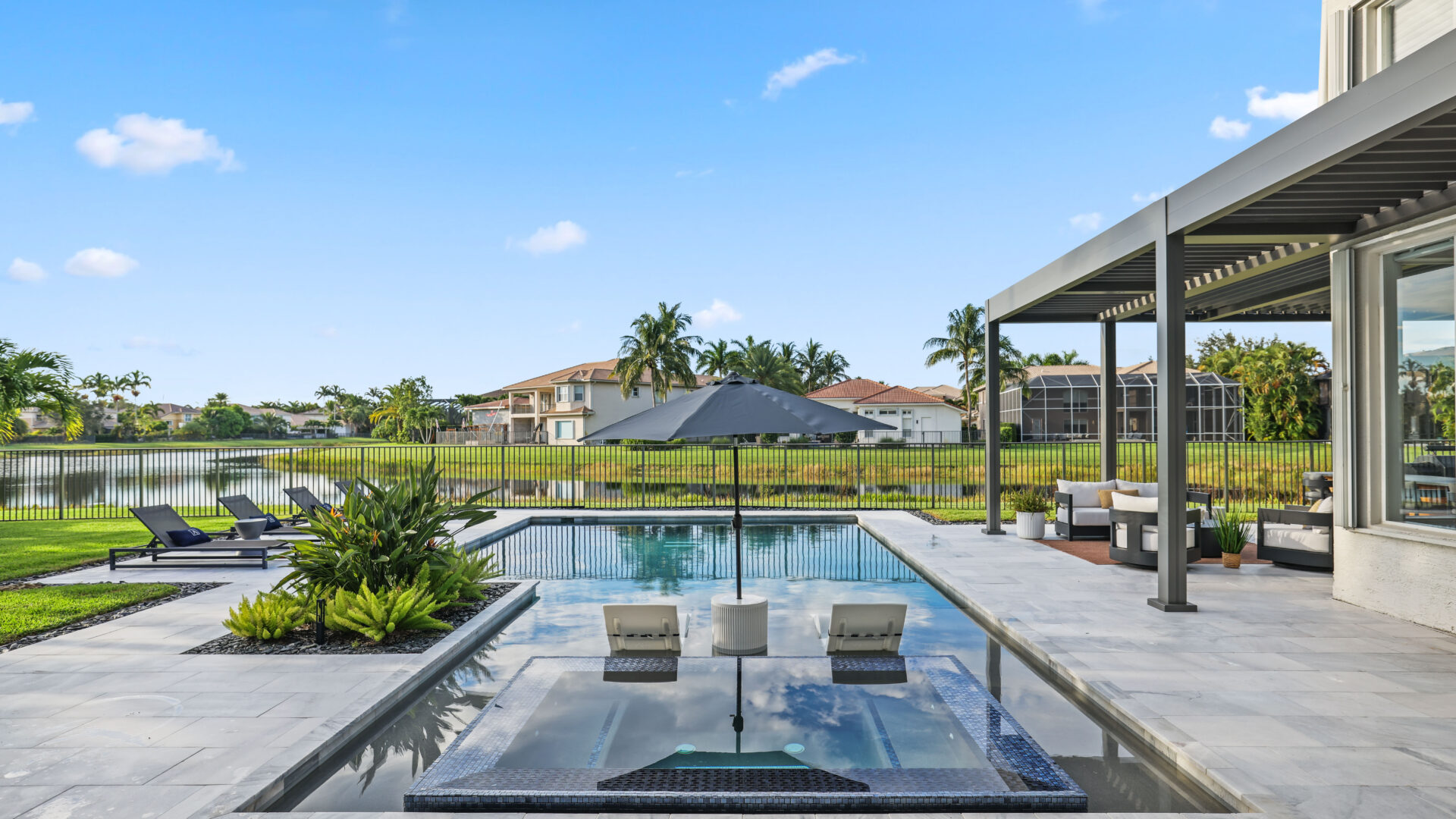 Modern pergola design overlooking a luxury pool and outdoor lounge area in a contemporary South Florida backyard.