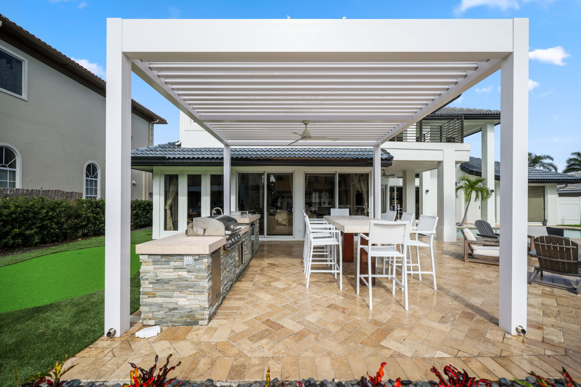 White aluminum pergola in Delray Beach shading an outdoor kitchen and bar with modern seating.
