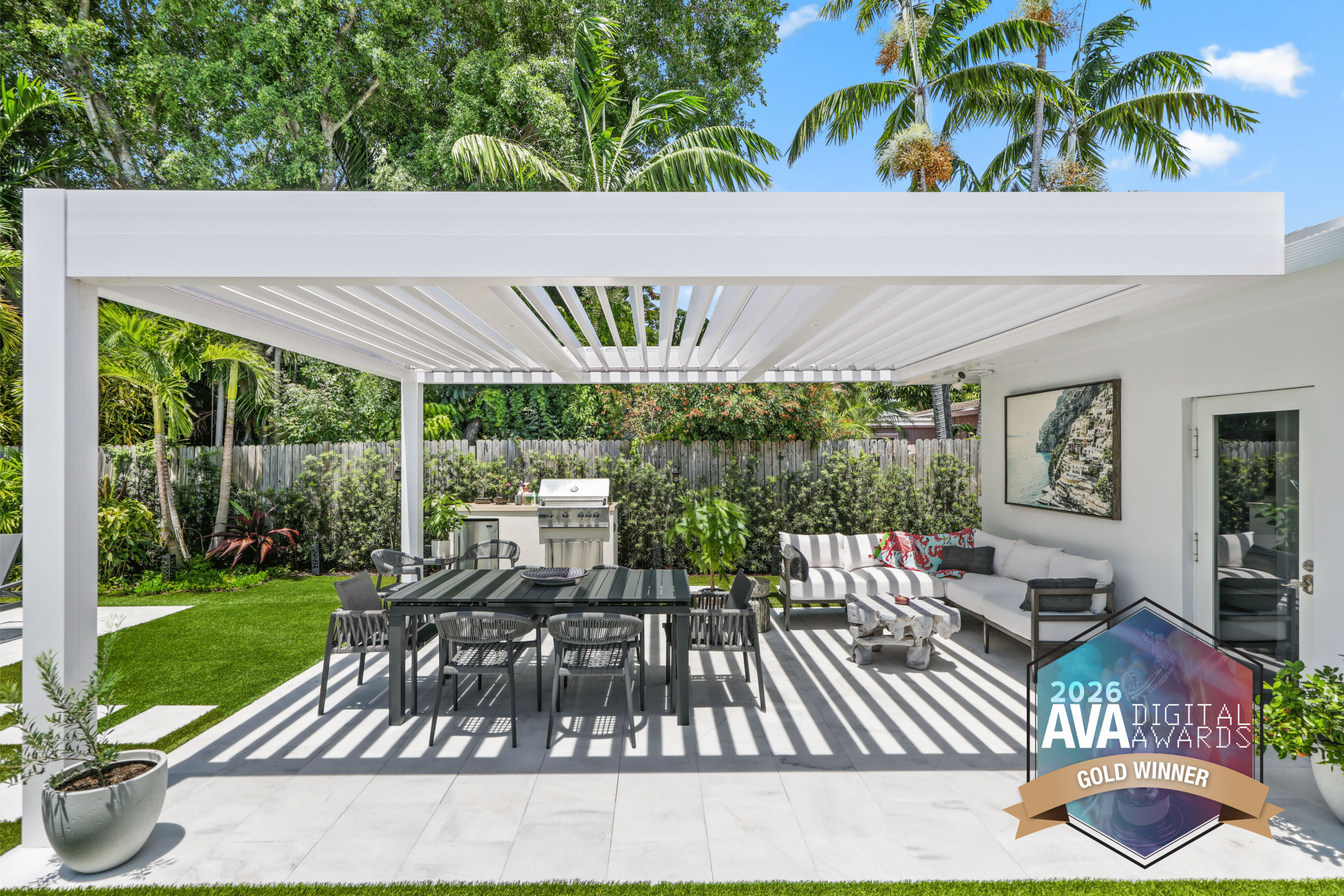 Luxury backyard dining space with white motorized pergola, outdoor kitchen, and modern lounge seating.