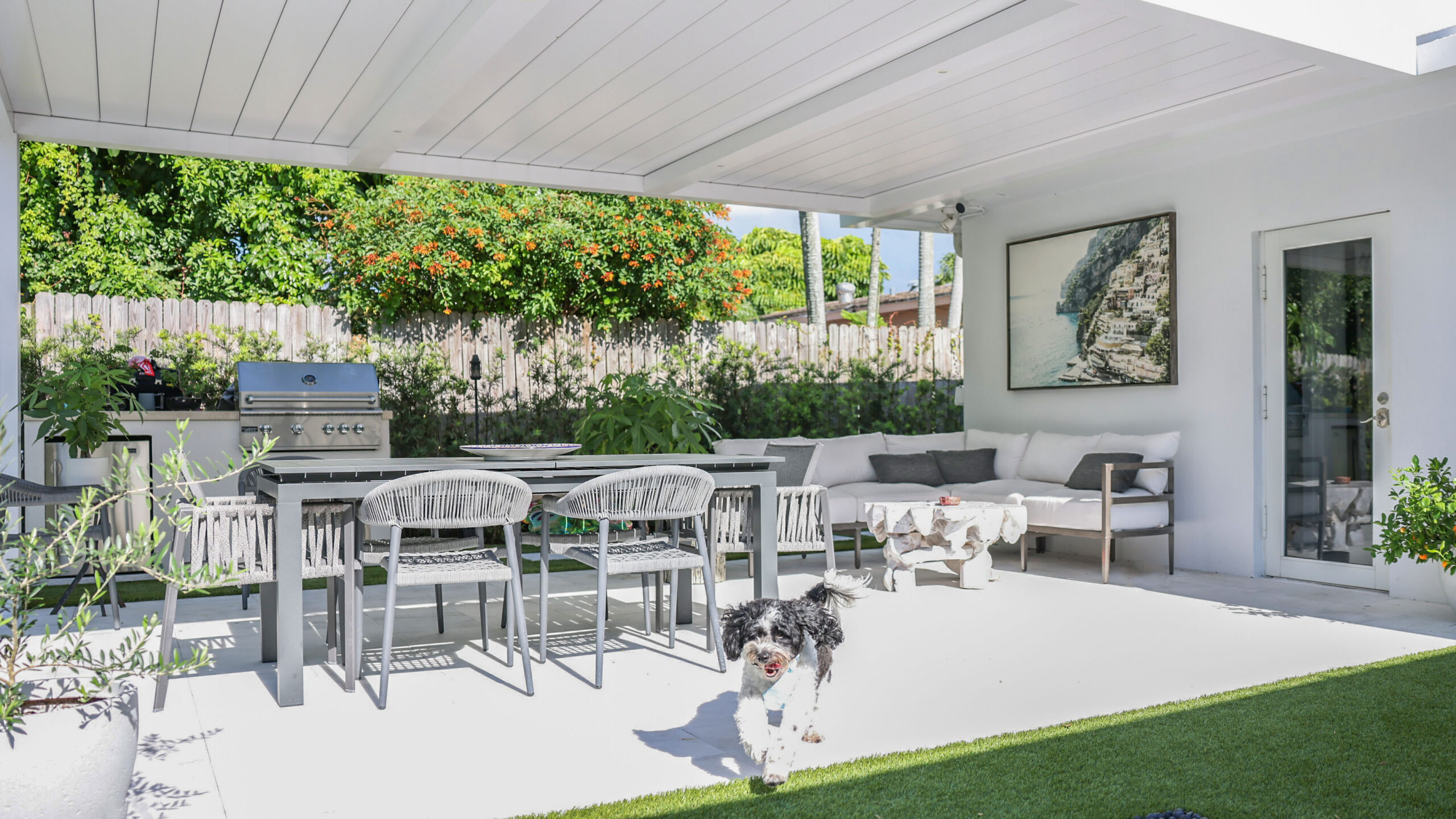 Covered outdoor living space with solid roof pavilion, dining area, lounge seating, and built-in grill.