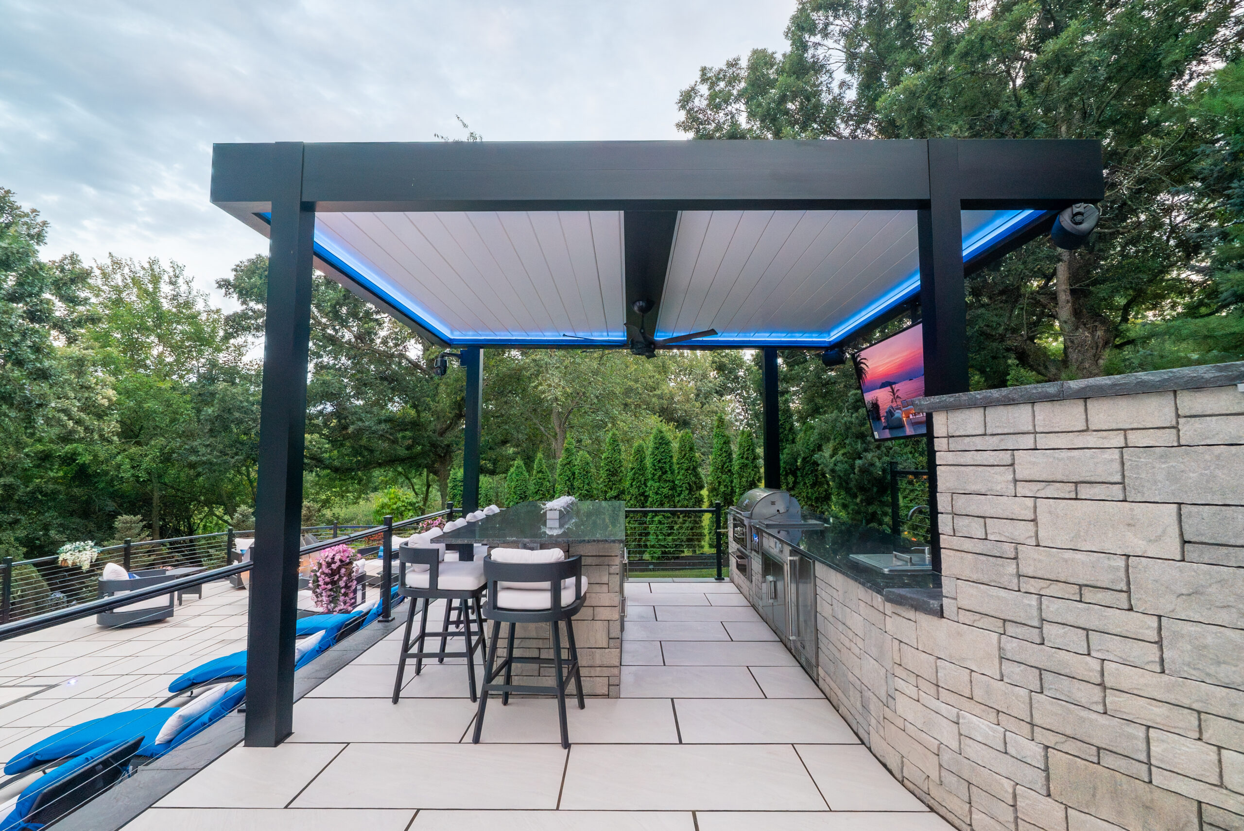 Modern pergola with integrated LED lighting over outdoor kitchen and bar, creating a sleek evening entertaining space.