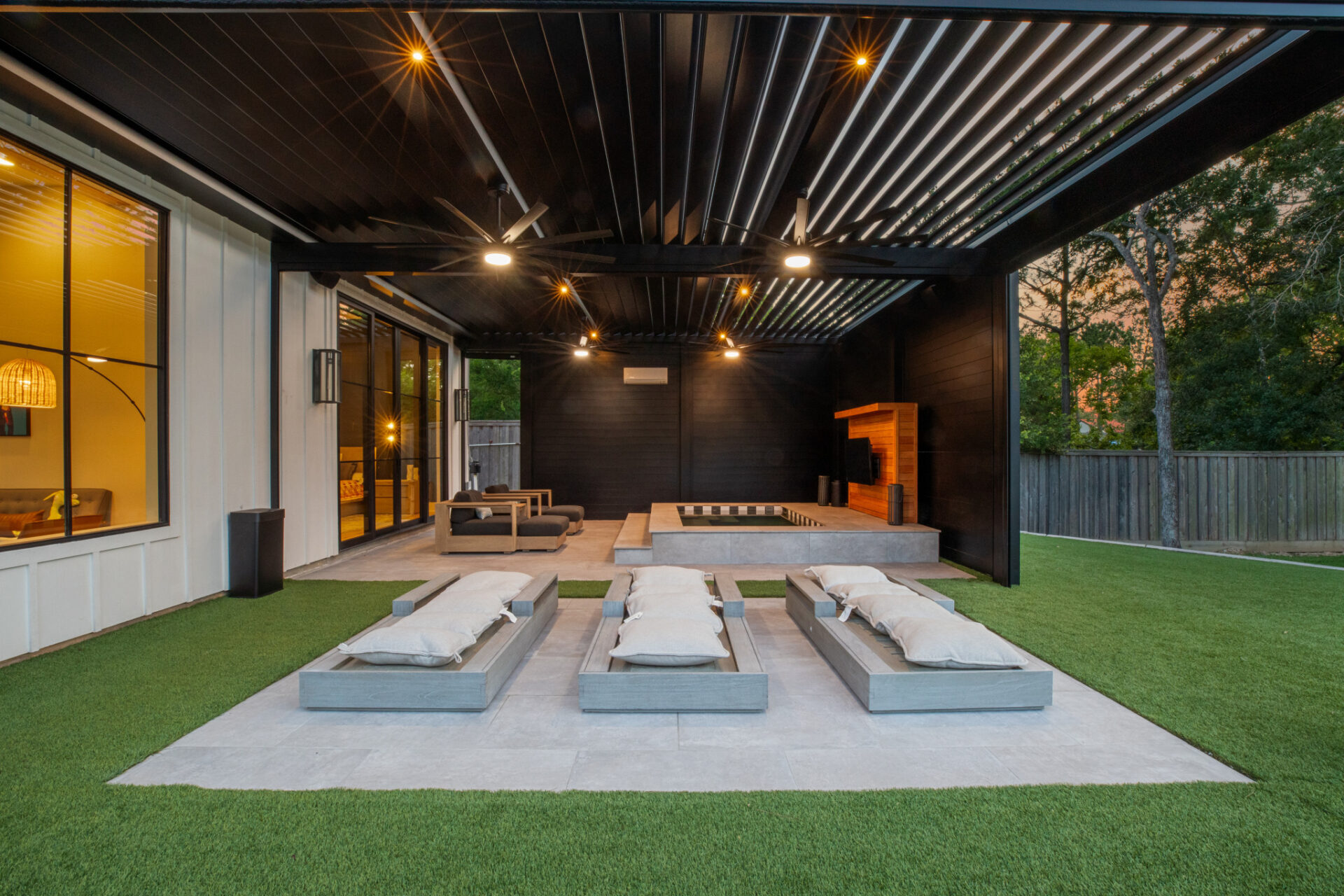 Modern pergola with integrated lighting, ceiling fans, and lounge seating, creating a luxurious backyard retreat at dusk.