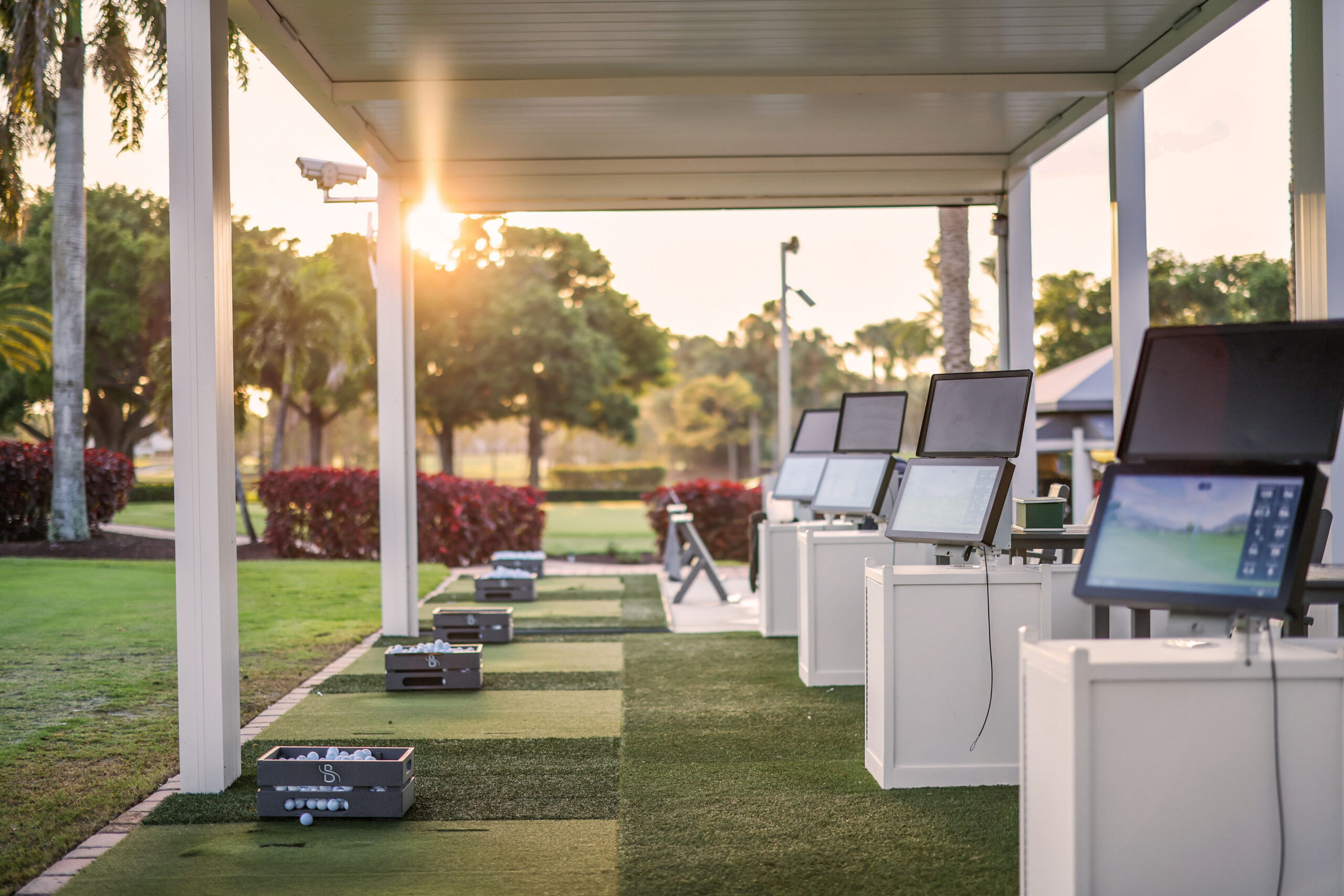 Golf simulator bay cover with launch monitors and shaded practice stations at private club.