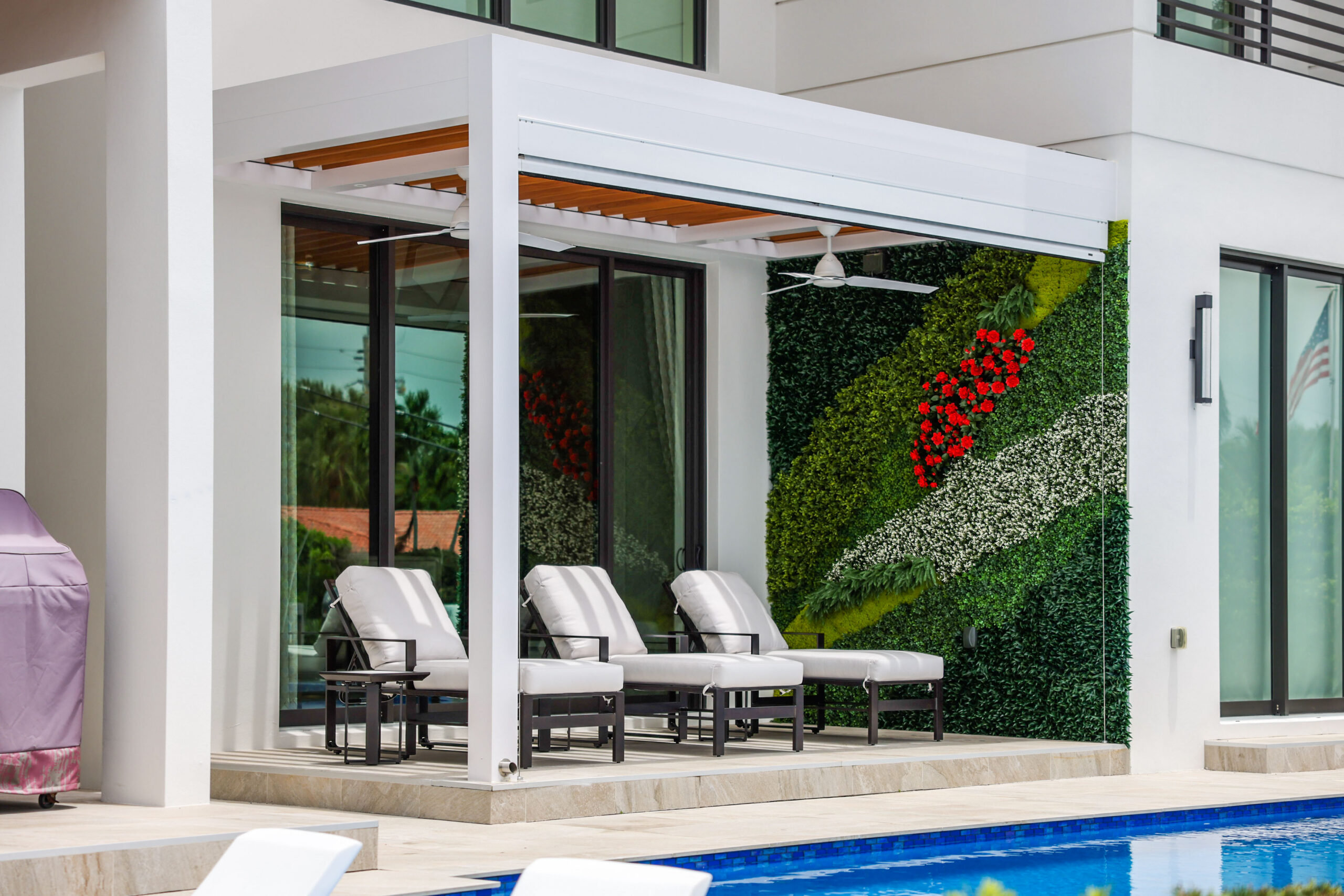Modern South Florida outdoor living area with covered pergola, poolside lounge chairs, and privacy green wall for shade and comfort.