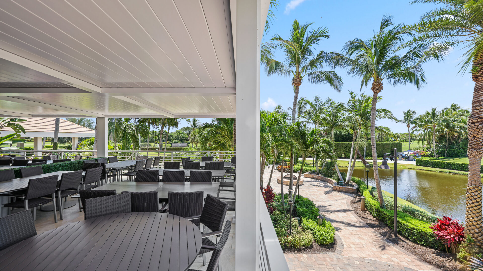 Luxury outdoor dining patio with aluminum pergola overlooking palm trees and water.