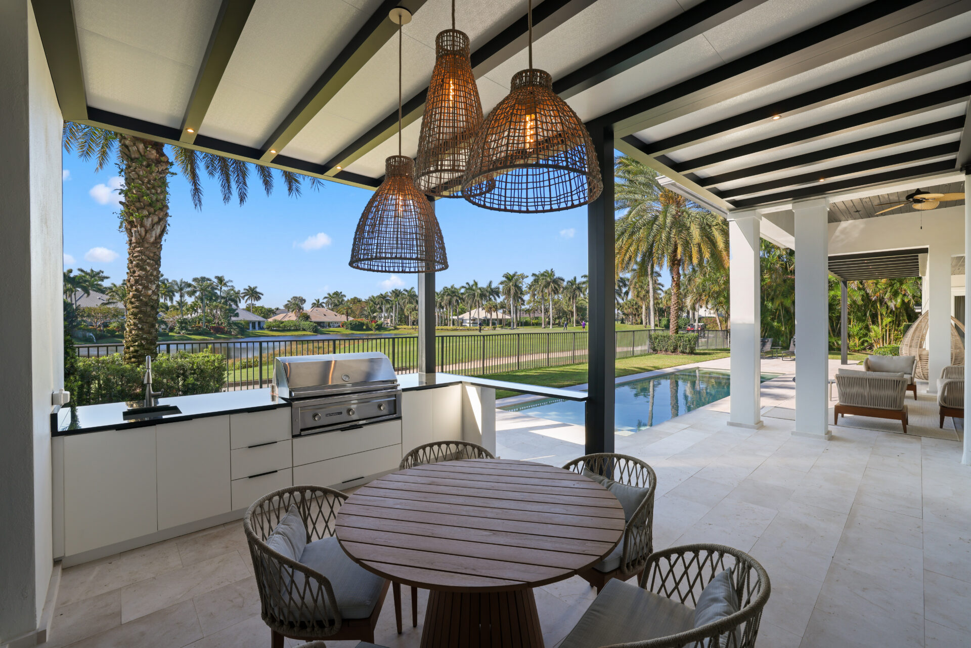 Outdoor kitchen under fixed roof pergola overlooking pool in South Florida backyard.