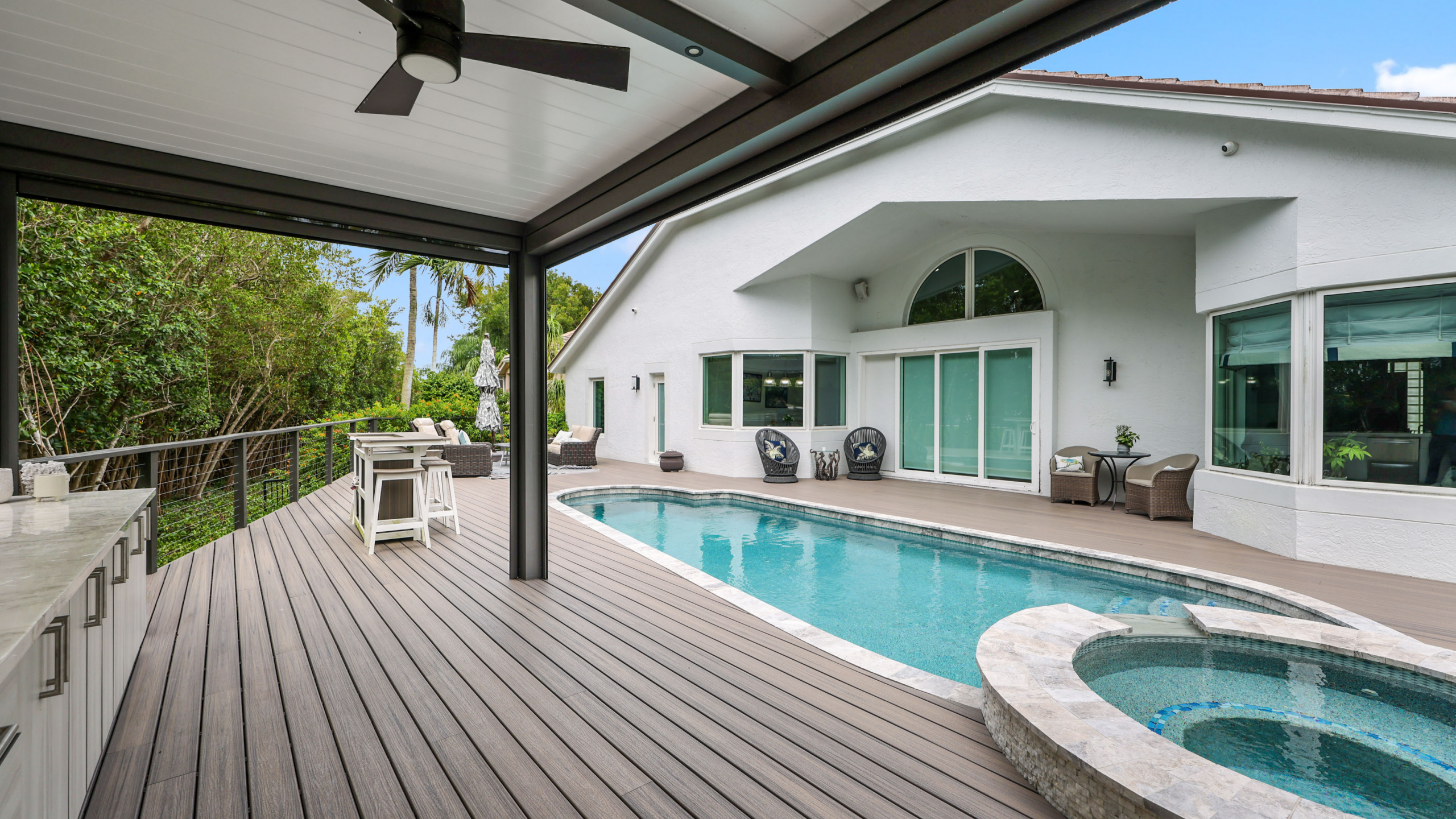 Covered backyard patio with pool, spa, ceiling fan, and outdoor kitchen seating area.