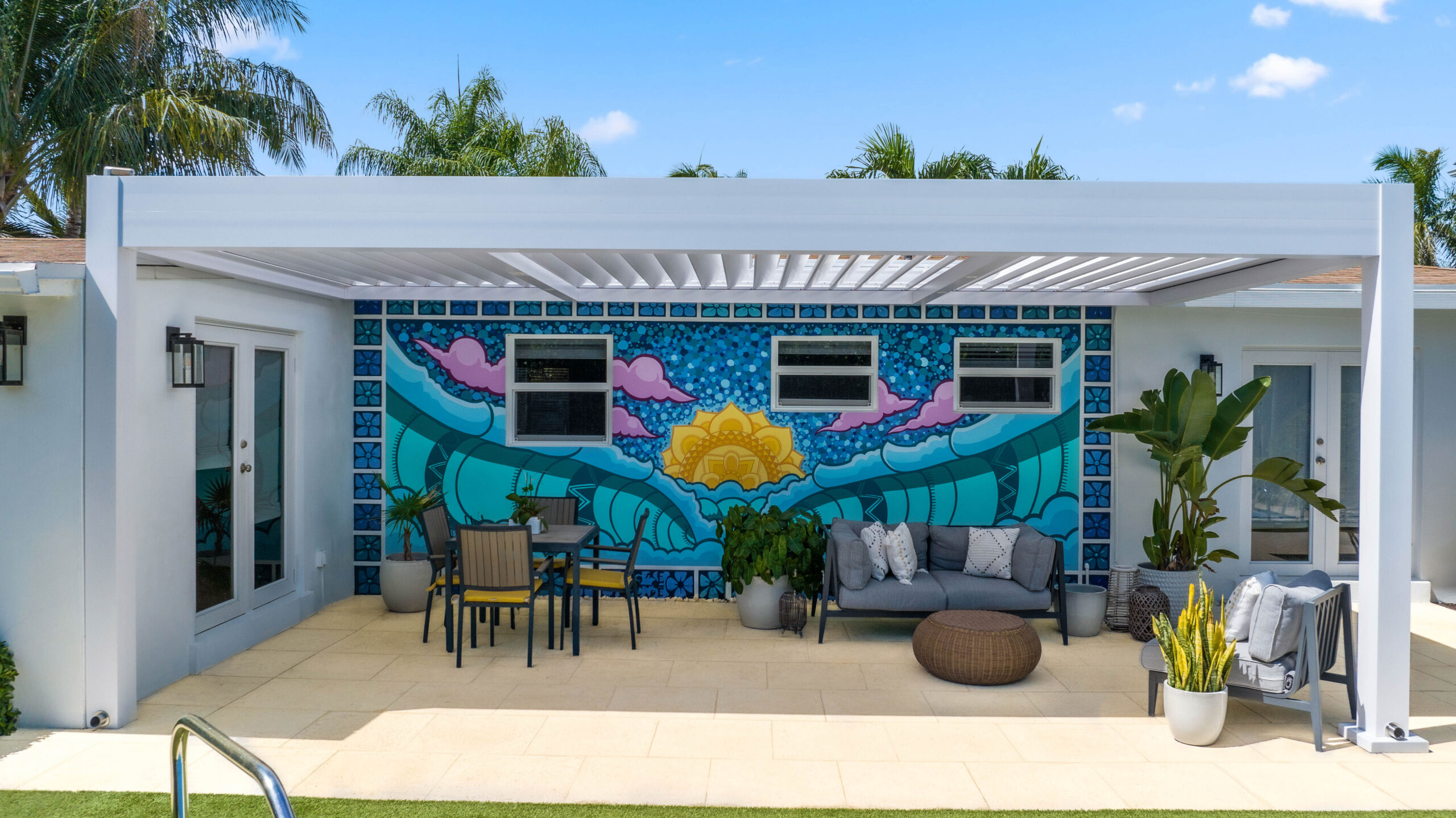 White louvered pergola over patio dining and lounge area with colorful mural in a modern backyard.