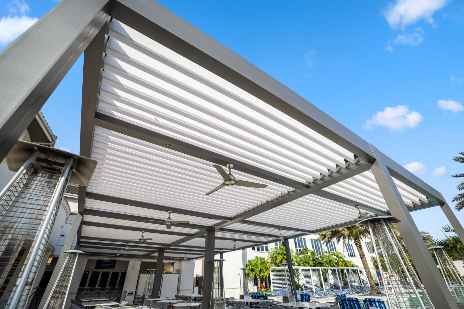 Motorized louvered pergola over restaurant patio seating with integrated fans and shade.